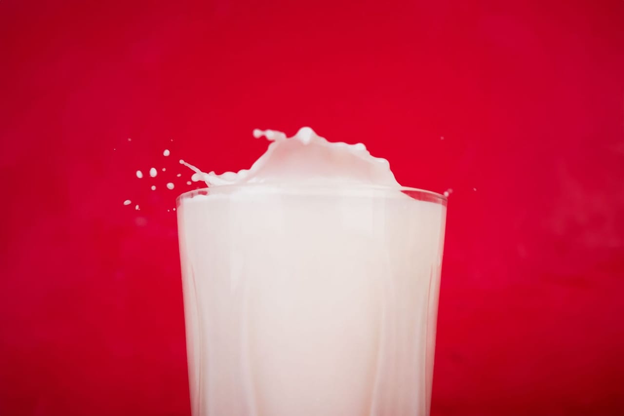 Glass of fresh milk splashing against a red background